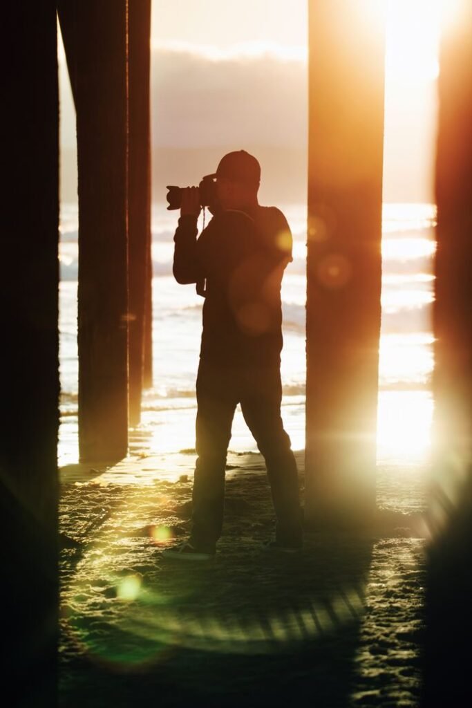 Silhouette of a photographer taking pictures at sunset under Pismo Beach Pier, California.